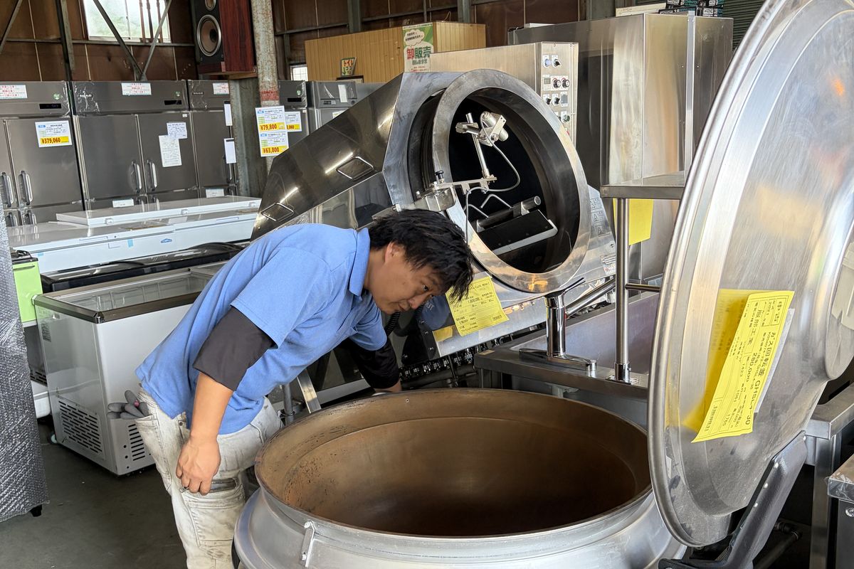 青いシャツのスタッフが回転釜の内部を点検している様子
